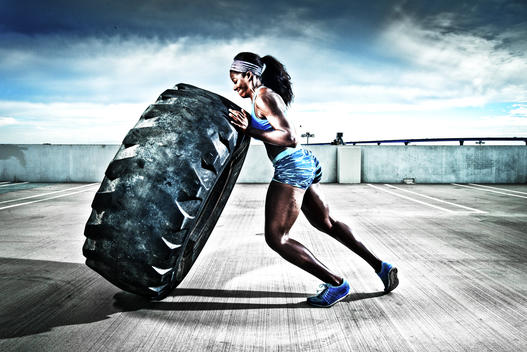 An athletic girl works out with a large tire.