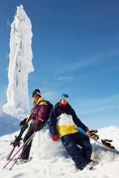 Snowboarder and skier at the top of mountain with equipment, in front of ice sculpture