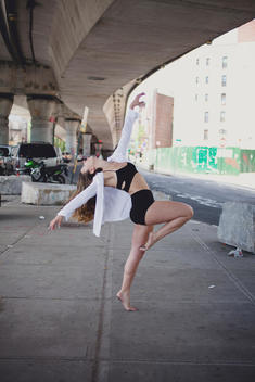 A young female dancer holding a dance pose under an overpass in New York City.