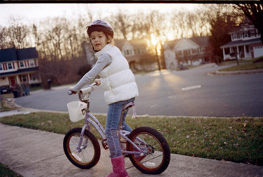 A young girl wearing a crash helmet on a bicycle in a suburban neighborhood