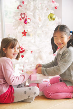 Two Young Girls Opening Presents under Christmas tree, Smiling