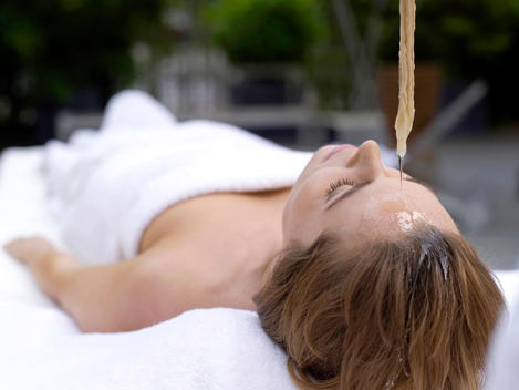 Young woman lying in spa with oil being poured on forehead, eyes closed