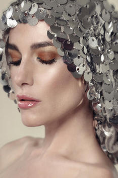 Close up beauty of caucasian woman. Wearing silver sequin headdress. With orange brown eyes & lipgloss. Looking down