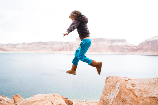 6 year old boy with blue pants jumping from rock to rock with lake Powell in the background.