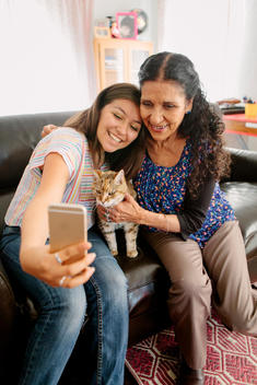 Grandmother and granddaughter taking selfie with cat on sofa