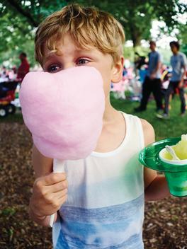 Boy in tank top eating cotton candy and flavored ice at summer festival.
