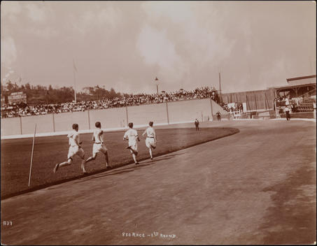 A Crowd Of Spectators Watch As Athletes Run On The Track At Manhattan Field.
