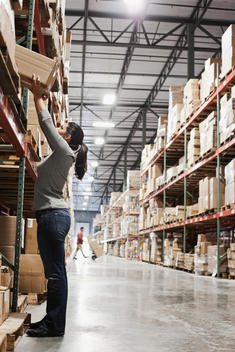Mixed race woman reaching for box in warehouse