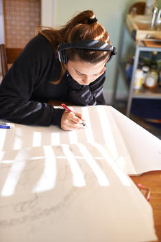 girl drawing with head phones on a sun lit table