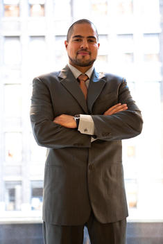 Young adult business man crossing his arms looking directly into the camera with a washed out background in the office.