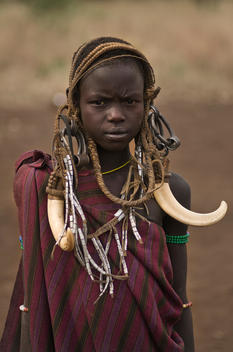 Mursi girl in Omo valley carrying large tusks from a wild boar for ornamentation