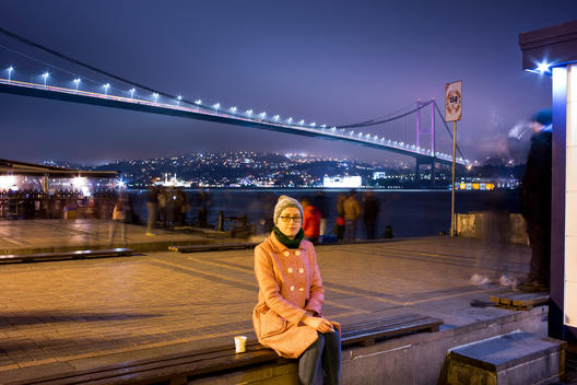 Young woman is smoking and drinking a coffee by the Bosphorus Bridge in the city of Istanbul.