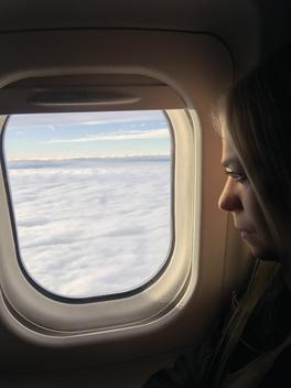 Self-portrait; Adult woman staring out of airplane window at clouds below.