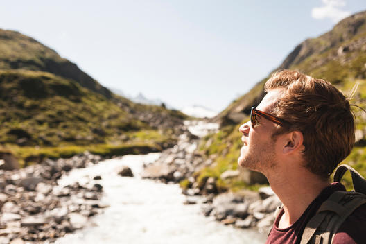 20 something man with sunglasses on and alpine river running behind him in the Austrian alps.