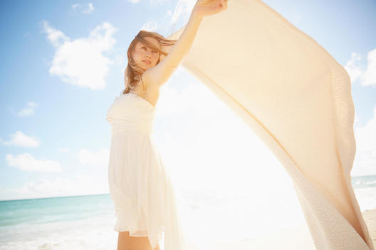 Caucasian woman holding blanket in wind on beach