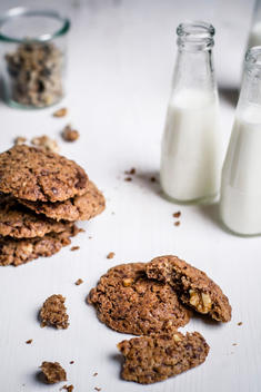 Bottles of milk with chocolate cookies and glass of walnuts on table, close up