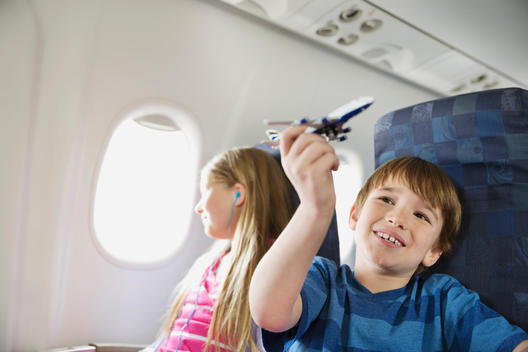 Boy playing with toy plane while sister listens to music in airplane