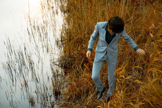 Man in suit walks through reeds by swamp.