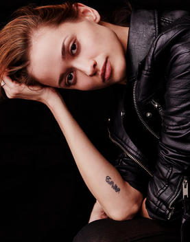 Woman in black leather jacket and a tattoo leaning on arm