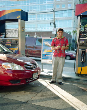 A Gas Station Attendant Counts Cash In A Colorful Red Shirt At A Gas Pump