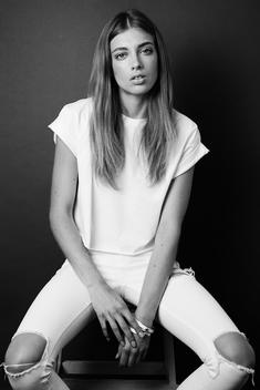 Model in studio sitting on stool wearing white jeans and a white top