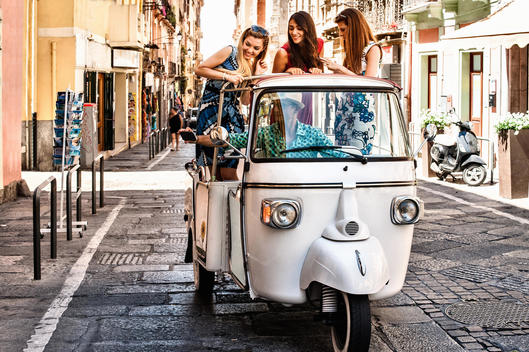 Three young women standing up in open back seat of Italian taxi, Cagliari, Sardinia, Italy