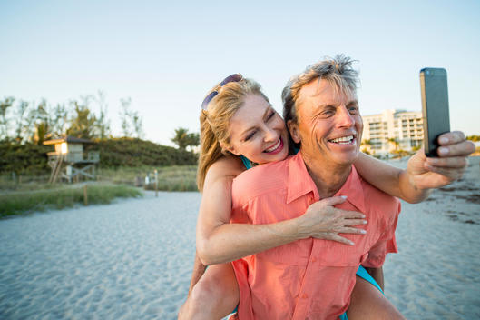 Older Caucasian couple taking cell phone selfie on beach