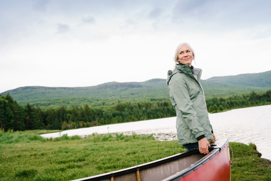 Portrait of a fit healthy older woman with grey silver hair standing near a lake and carrying a canoe.