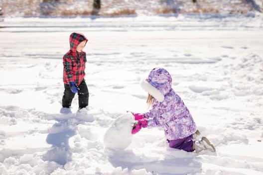 A girl and her brother make a snowman in the snow after a snowstorm in her suburban neighborhood. Denver, Colorado