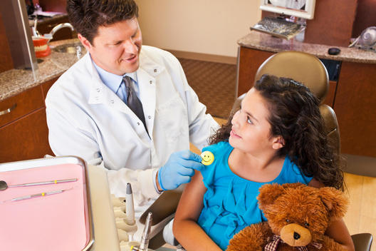 Dentist pinning smiley face badge on girl in dentist's chair