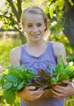 Smiling young girl standing in a garden holding a basket of leafy vegetables