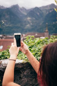 Over shoulder view of teenage girl with henna tattoo using smartphone to photograph mountain range, Bludenz, Vorarlberg, Austria