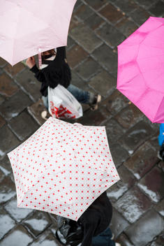 Overhead view of people walking with umbrellas over wet cobblestones