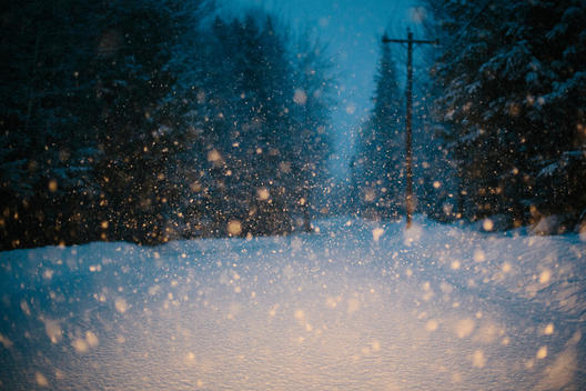 Snow squall lit by headlights on a snow covered road at dusk.