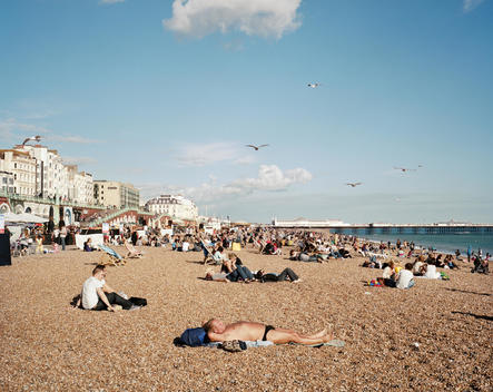 Tourists and residents lie on Brighton beach in summer. Brighton Pier can be seen in the distance.