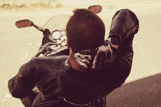 A motorcycle rider with a leather suit resting on his bike with his back turned