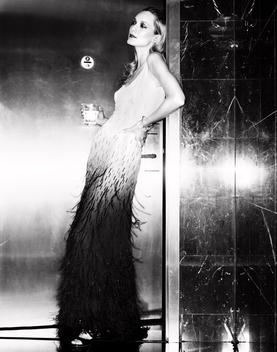 A model standing in the doorway having a cocktail in a long evening dress.