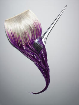 Weft of white hair being dyed purple with a clear tint brush.