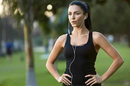 Mid adult woman wearing earphones, hands on hips
