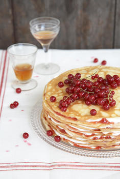 Layered Crepes On White Table Cloth With Currants And Glasses Of Apperitif.