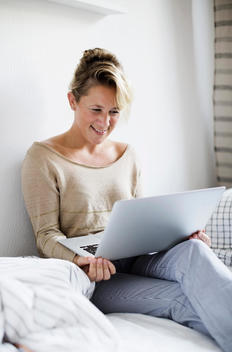 Happy woman using laptop in bed at home