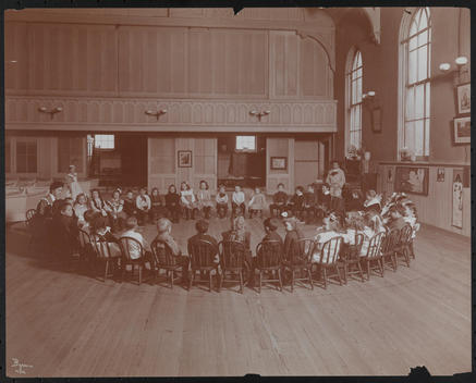Group Of Young Boys And Girls Seated In Chairs Arranged In A Circle, With Teachers, At Christ Church.