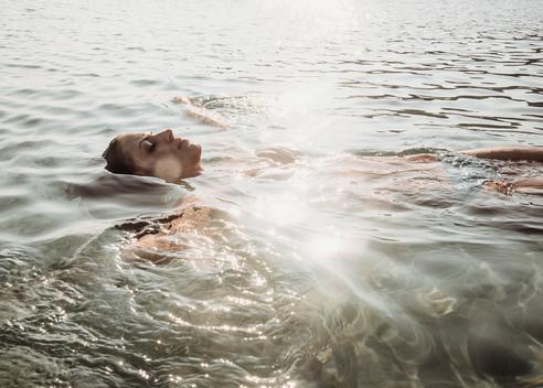 Beautiful young woman floating in sunlit sea