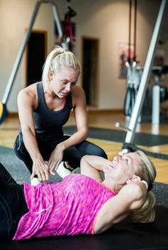 Female instructor assisting senior woman in doing sit-ups at gym
