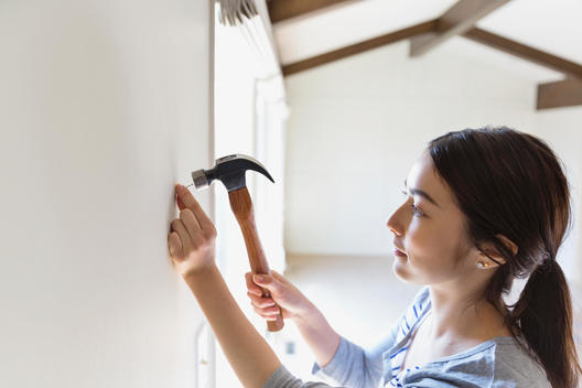 Young woman hammering nail into wall at home