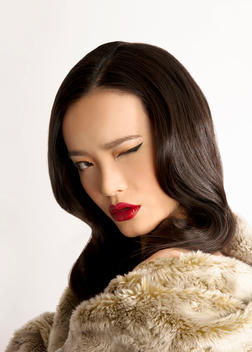 Beauty shot of an Asian woman wearing fur, red lips, one eye closed.