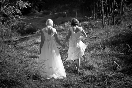 Friends Wearing White Dresses And Walking Hand In Hand Through A Meadow, New York City, New York State, Usa.