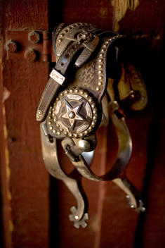 Pair of spurs hanging on a red barn wall.
