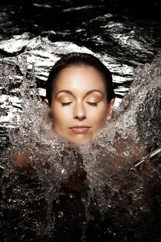 Caucasian woman in her 20's with eyes closed submerged to her neck and water cascading in around her neck
