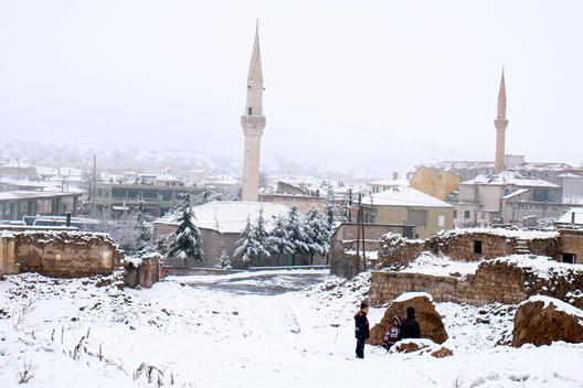 General view from snowy Cappadocia where fairy chimneys are exist, children are playing around ruined houses.